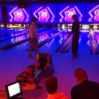 Gruppe von Personen beim Bowling in einer neonbeleuchteten Halle mit futuristischen Lichtinstallationen auf den Leinwänden über den Bahnen.
