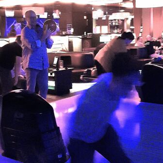 Zwei Personen beim Bowling in neonbeleuchteter Halle, eine hält eine Kugel, die andere läuft vorbei.