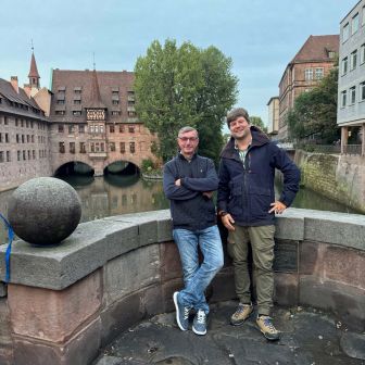 Zwei Mitarbeiter stehen an einer Mauer in Nürnberg. Im Hintergrund Wasser.